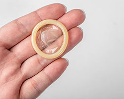 A hand holding a rolled up condom against a white background