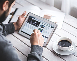 A man reading information on his tablet, with a cup of coffee