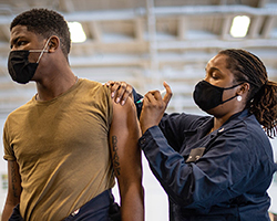 Two workers from the Navy wearing masks to protect from COVID while getting/giving flu shots.