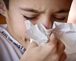 a kid blowing their nose into a tissue