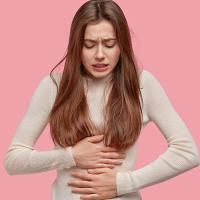 A woman clutching her abdomen, experiencing period cramps.