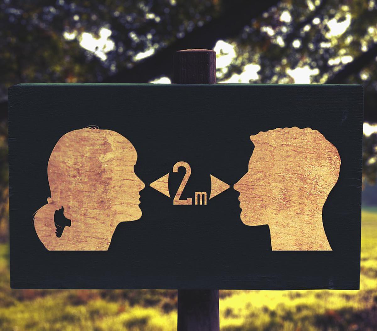 A sign for social distancing at a park, showing two people's faces, with a measurement of 2m recommended between them.