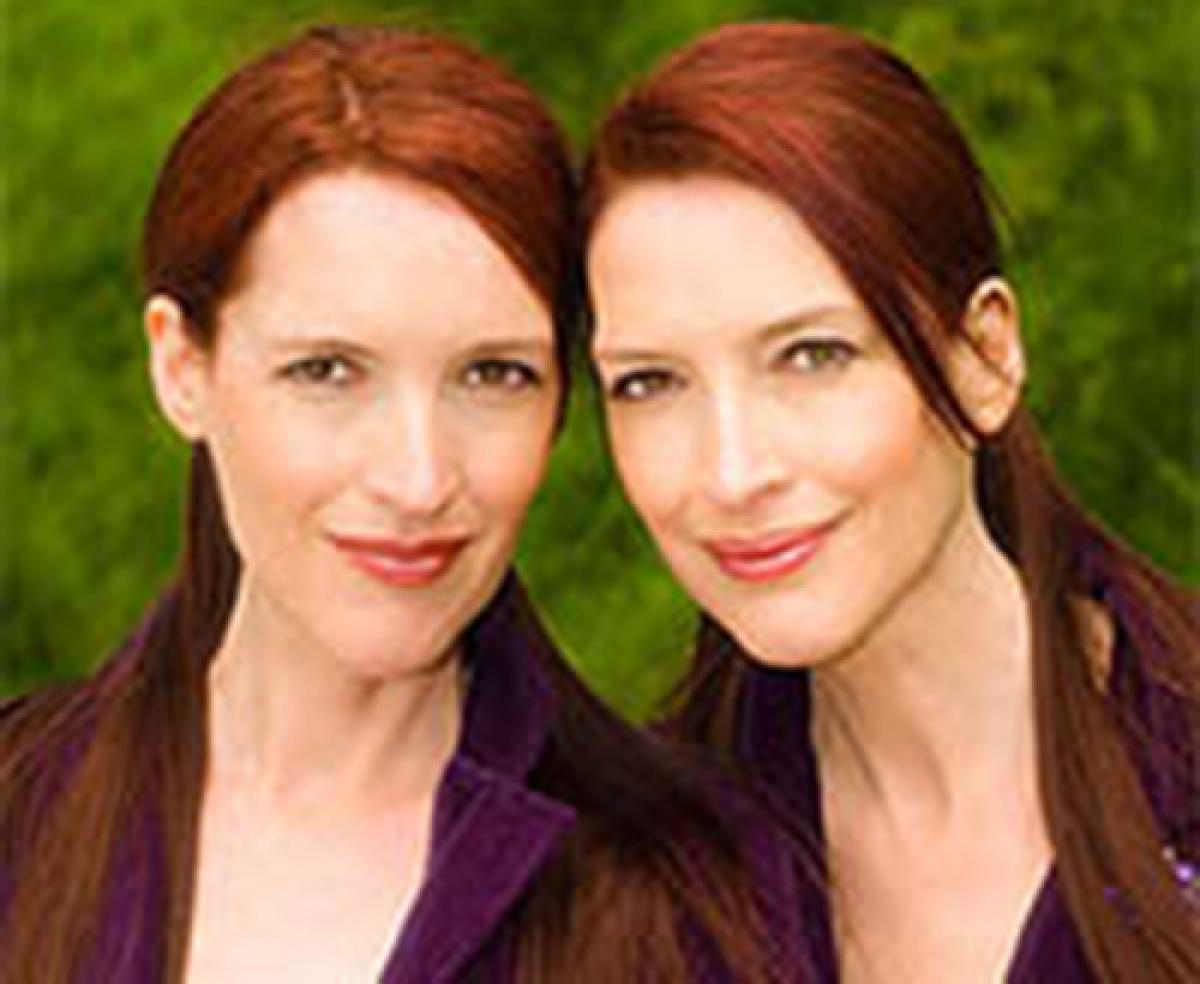 An image of adult twin sisters with red hair, dressed in purple